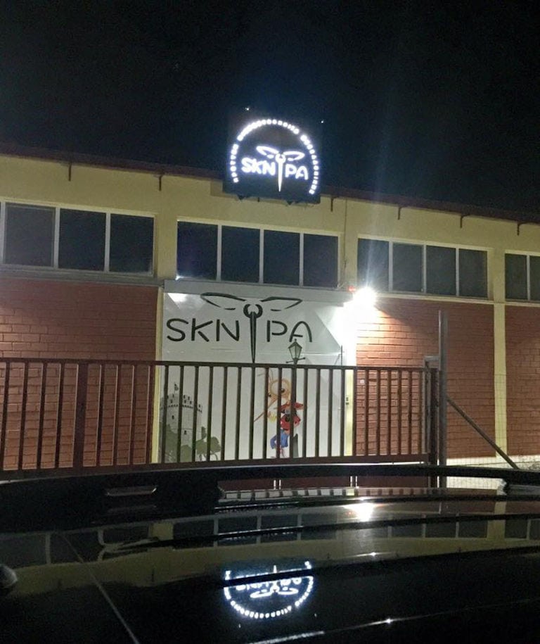 front view by night of the building that says 'SKNIPA' on illumitated panel in upper part of the wall